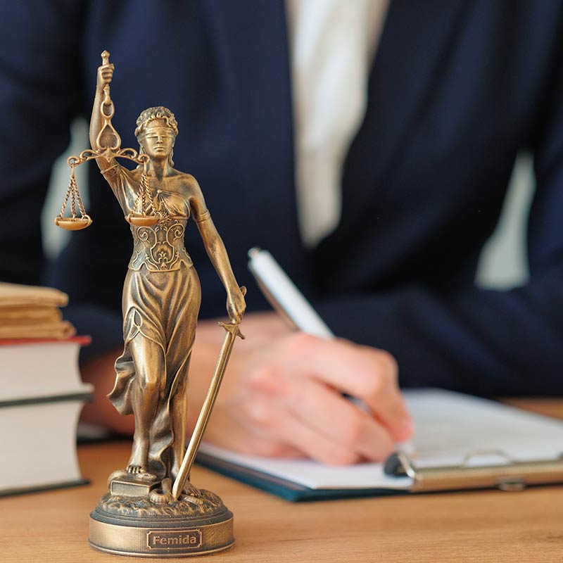 Juriste prenant des notes avec la statue de Thémis à ses côtés, symbole de la justice